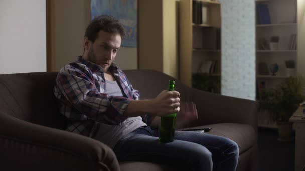 Drunk male sitting on couch and talking to bottle of beer, addiction to alcohol - Felvétel, videó