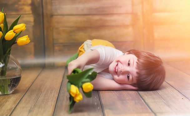 A small child with a bouquet of yellow tulips. A boy with a gift - Zdjęcie, obraz