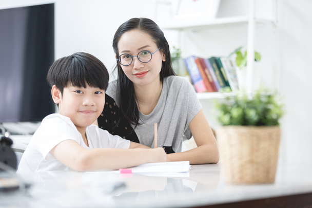 Asiático chico con madre enseñando y aprendiendo su tarea en casa
 - Foto, imagen
