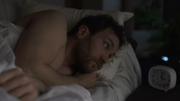 Kerl, der sich im Bett dreht, nicht einschlafen kann, wütend auf die Uhr schaut, Schlaflosigkeit - Filmmaterial, Video