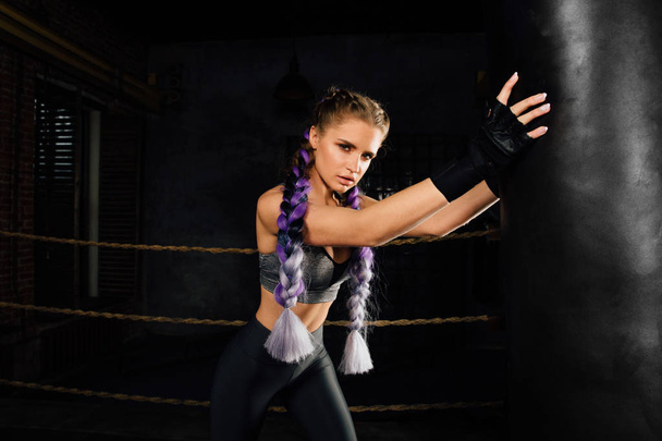 Young woman trains in boxing ring with heavy punching bag. - 写真・画像
