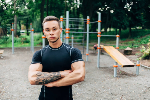 Jovem atleta caucasiano em sportwear preto e tatuagens, treinando ao ar livre e posando
 - Foto, Imagem