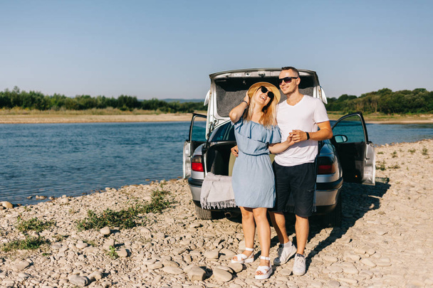 Happy traveler couple standing near car open trunk and watch the sunrise - Fotografie, Obrázek
