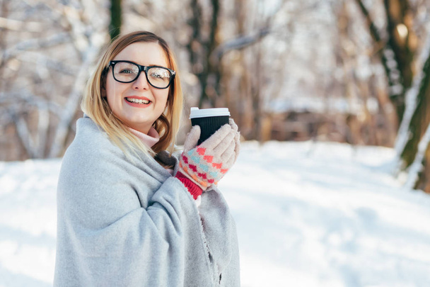 ピンクのセーターとニットのスカーフで若い白人魅力的なブロンドの女の子が屋外冬の公園でのコーヒーのカップを保持します。 - 写真・画像