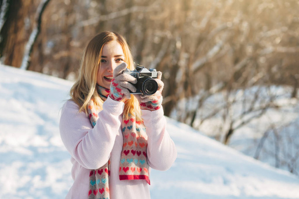 Giovane caucasico attraente ragazza bionda in maglione rosa e sciarpa lavorata a maglia tiene macchina fotografica film retrò nel parco invernale all'aperto
 - Foto, immagini