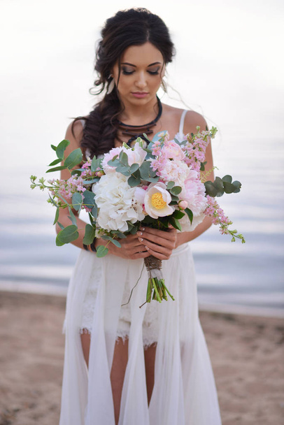 bride in a boho style on the beach near the sea with a wedding bouquet - Fotó, kép