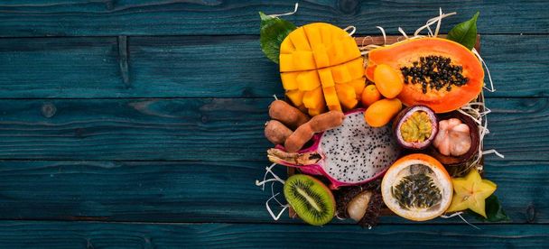 Fruit dragon, papaya, maracuya, kiwi, mango and granadilla in a wooden box. Fresh Tropical Fruits. On a wooden background. Top view. Copy space. - Foto, imagen