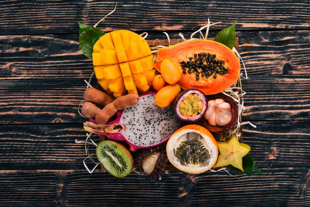 Fruit dragon, papaya, maracuya, kiwi, mango and granadilla in a wooden box. Fresh Tropical Fruits. On a wooden background. Top view. Copy space. - Foto, imagen