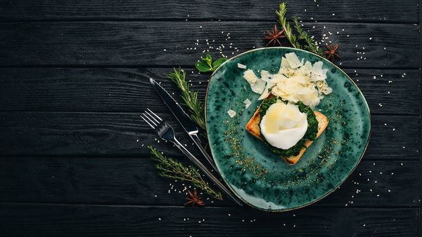 Breakfast. Toast Bread with Spinach, Poached Egg and Parmesan Cheese. On a black wooden background. Copy space. - Φωτογραφία, εικόνα