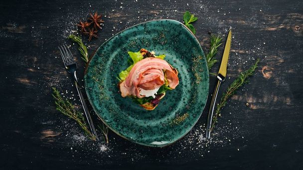 Breakfast. Poached egg, bacon on lettuce made from toast. On a black wooden background. Copy space. - Fotografie, Obrázek