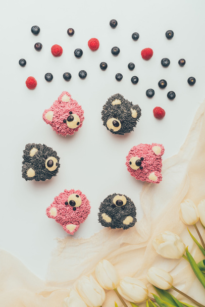 Blick von oben auf Gourmet-Cupcakes in Form von Bären, frischen Beeren und Tulpenblumen   - Foto, Bild