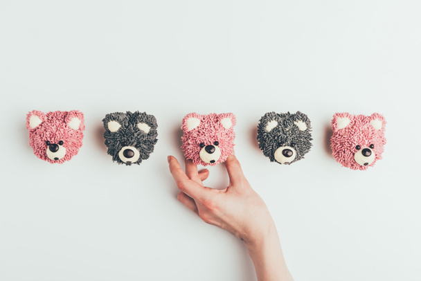 cropped shot of human hand and delicious muffins in shape of bears isolated on grey   - Фото, изображение