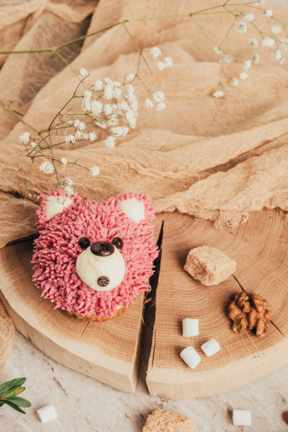 top view of sweet pink muffin in shape of bear and nuts with sugar on wooden board - Photo, Image