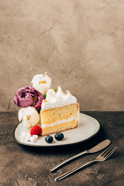 leckeres Stück Kuchen mit Schlagsahne, frischen Beeren und Tulpen auf dem Teller - Foto, Bild