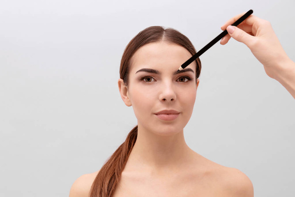 Young woman undergoing eyebrow correction procedure on light background - Zdjęcie, obraz