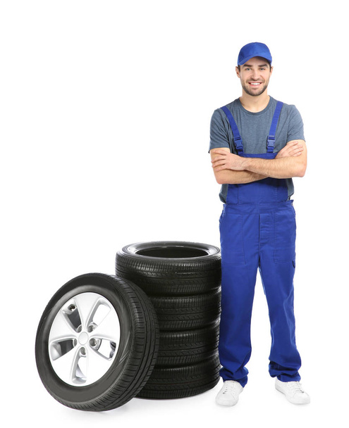 Young mechanic in uniform with car tires on white background - Photo, image