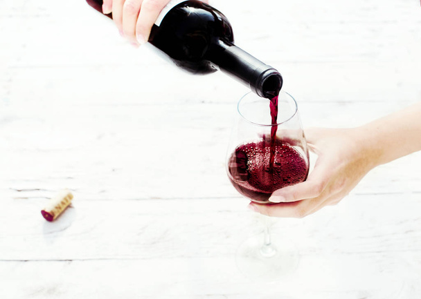 Woman hand Pouring red  wine from bottle into the wine glass on white wooden background with copyspace - Foto, Imagen