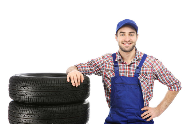 Young mechanic in uniform with car tires on white background - Fotoğraf, Görsel