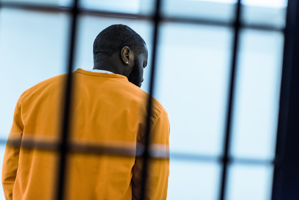 vista trasera del prisionero afroamericano tras las rejas de la prisión
 - Foto, imagen