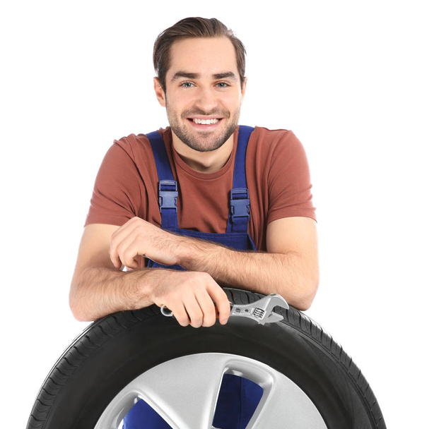 Young mechanic in uniform with car tire on white background - Foto, Bild