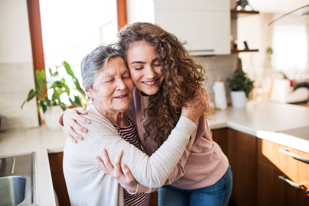 ein Teenager-Mädchen mit Großmutter zu Hause, umarmt. - Foto, Bild