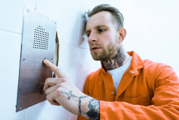 татуйований злочинець в помаранчевій формі натискання кнопки в камері в'язниці
 - Фото, зображення
