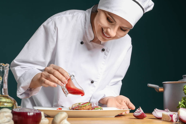 Female chef in uniform adding sauce to tasty dish on table - Photo, Image
