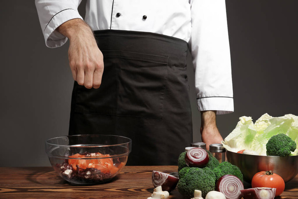 Male chef in uniform adding spices to tasty dish on table, closeup - Fotoğraf, Görsel