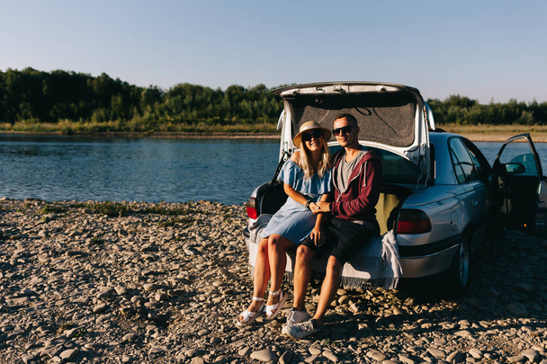 Ευτυχισμένος ταξιδιώτης ζευγάρι στέκεται κοντά σε αυτοκίνητο άνοιγμα κορμού και να παρακολουθήσετε την Ανατολή του ηλίου - Φωτογραφία, εικόνα