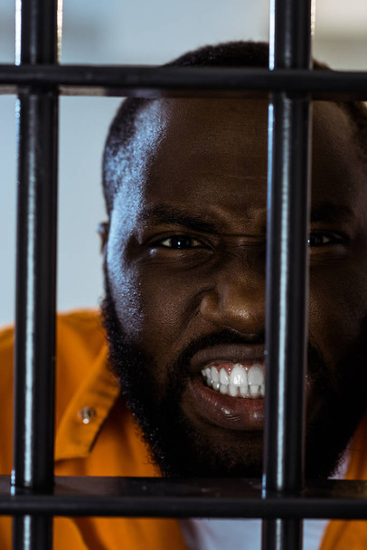 επιθετική αφρικανική αμερικανική αιχμάλωτος πίσω από τα κάγκελα της φυλακής - Φωτογραφία, εικόνα