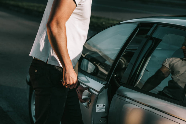 Молодий привабливий білий чоловік у білій футболці, що стоїть біля машини
 - Фото, зображення