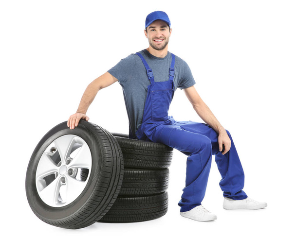 Young mechanic in uniform with car tires on white background - Foto, Imagen