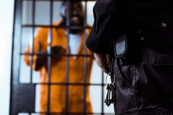 image recadrée du garde de sécurité debout près des barreaux de prison avec des clés
 - Photo, image