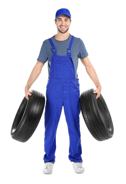 Young mechanic in uniform with car tires on white background - Foto, immagini