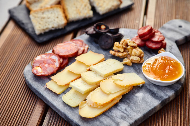 様々 なチーズのセット スモーク ソーセージ、アプリコット オレンジ ソース、クルミ、血のソーセージと揚げパン大理石ボードと木製のテーブル. - 写真・画像