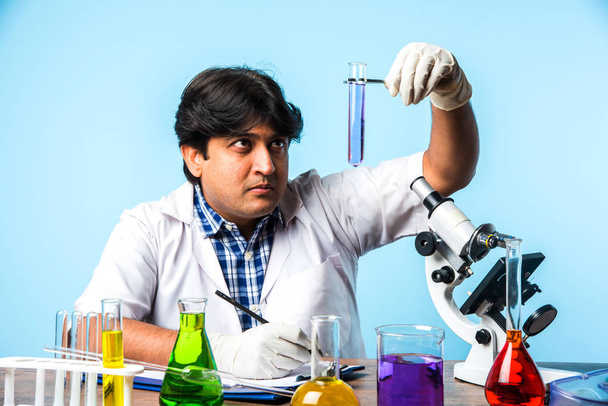 Asiático / Indiano cientista masculino ou médico ou estudante de ciências experimentando microscópio e produtos químicos, laptop e smartphone em um laboratório
 - Foto, Imagem