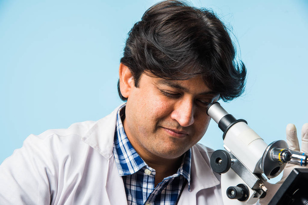 Científico o o médico asiático / indio o estudiante de ciencias experimentando con microscopio y productos químicos, computadora portátil y teléfono inteligente en un laboratorio
 - Foto, Imagen