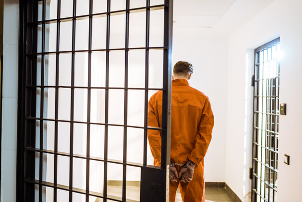 visão traseira do prisioneiro de pé algemado no corredor
 - Foto, Imagem