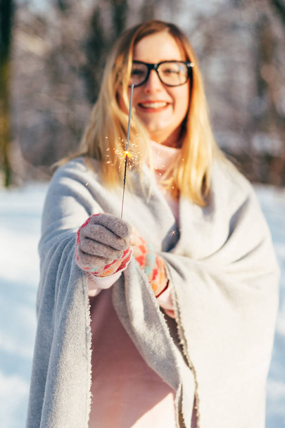 Young caucasian attractive blonde girl in pink sweater and knitted scarf holds bengal lights in winter park outdoor - Fotografie, Obrázek