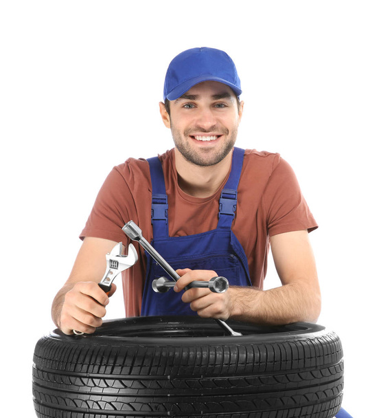 Young mechanic in uniform with car tire on white background - Фото, изображение