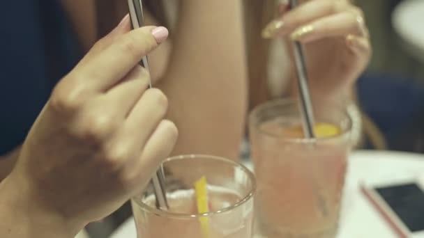 Two women drinking cocktails at a bar with a tilt up view from the drinks and straws to their faces. - Felvétel, videó