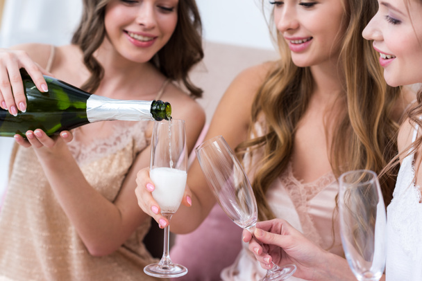 Schnappschuss von schön lächelnden Freundinnen im Pyjama, die Champagner in Gläser gießen - Foto, Bild