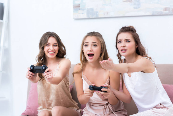 mujeres jóvenes emocionales en pijama jugando con joysticks juntos en casa
 - Foto, Imagen
