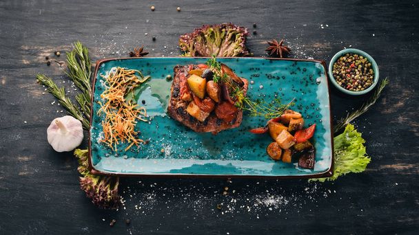Pork steak grilled with vegetables. Hot appetizers. Top view. On a black wooden background. Copy space. - Foto, Bild