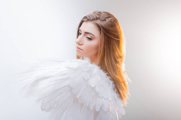 Jonge, prachtige blonde meisje in de afbeelding van een engel met witte vleugels. - Foto, afbeelding