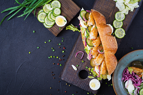 Sanduíche de baguete com peixe, ovo, cebola em conserva e folhas de alface. Vista superior
 - Foto, Imagem