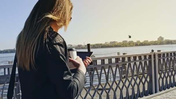 Young professional woman walking across a pedestrian walkway with her tablet and cup of coffee tilting down to her legs as she walks. - Video