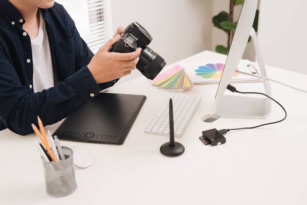 Αρσενικό φωτογράφος που κάθεται στο γραφείο του, ψάχνει για φωτογραφική μηχανή - Φωτογραφία, εικόνα
