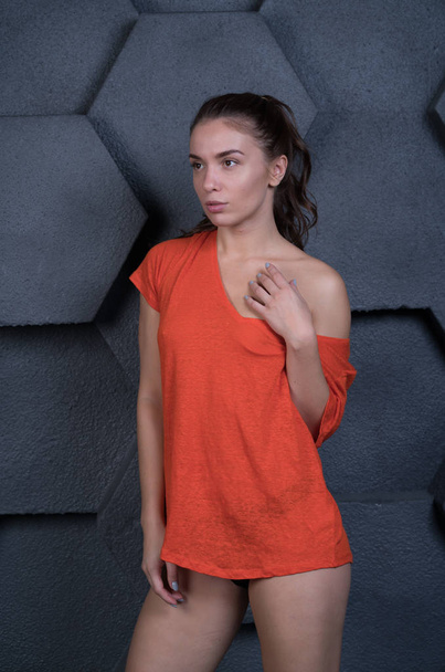 young beautiful girl posing in studio in an orange t-shirt - Фото, изображение