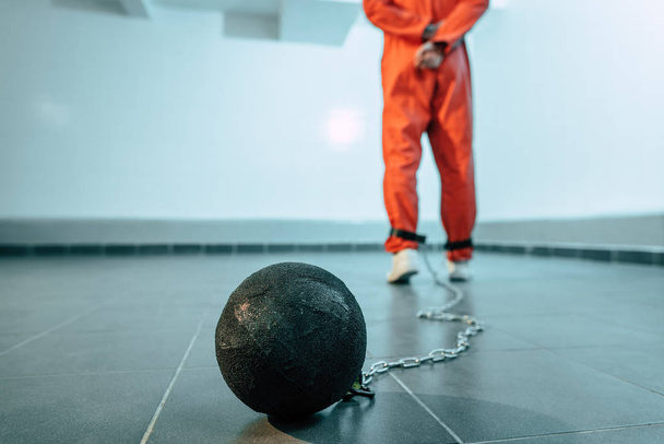 back view of prisoner in orange uniform with weight tethered to leg - Φωτογραφία, εικόνα